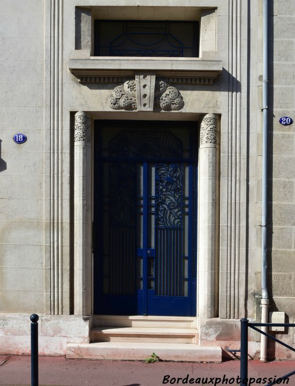 La porte en ferronnerie très Art Déco est encadrée par deux piliers au chapiteau stylisé.