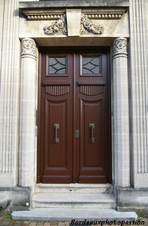 Porte  encadrée par des cannelures et deux colonnes à facettes avec chapiteaux cylindriques de fleurs stylisées.